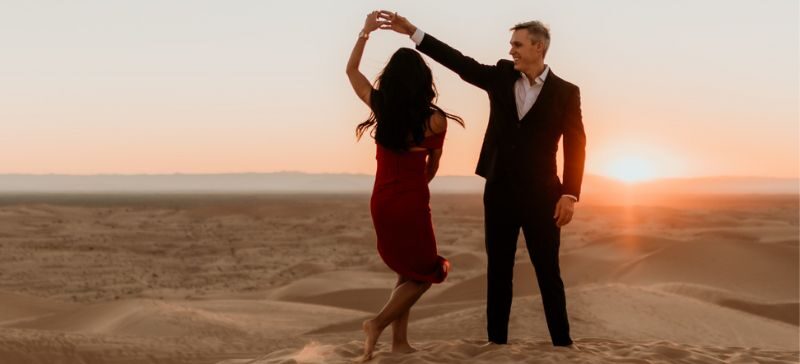 man and woman doing a waltz in the desert at sunset