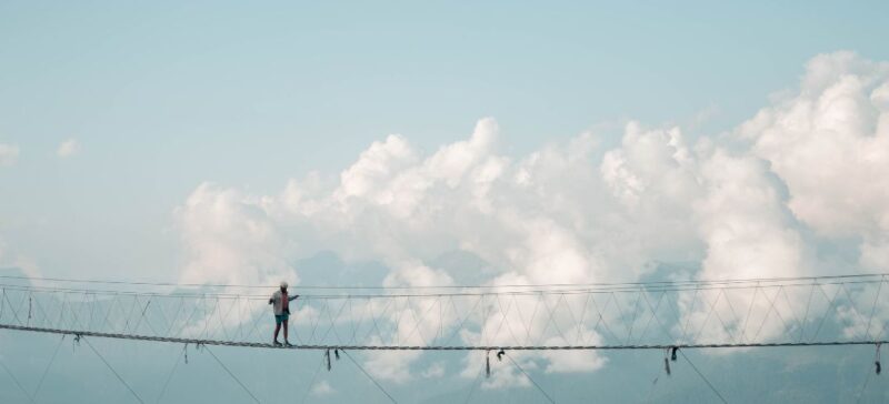 a person walks a tight rope very far off the ground with blue sky and clouds in the background