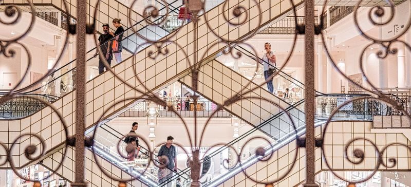 looking through ornate metal bars at holiday shoppers ride escalators in a mall
