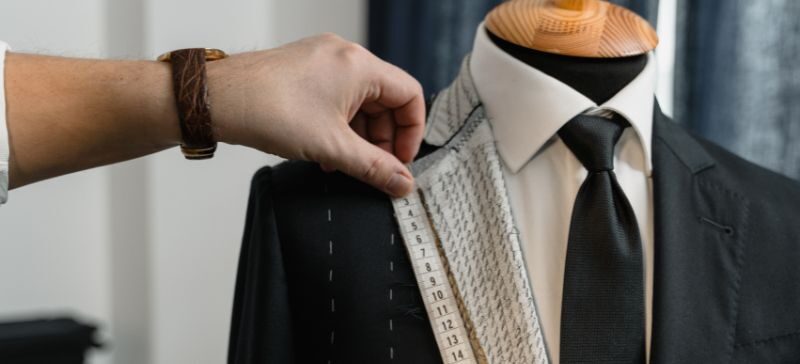 A tailor measures the lapel of a blazer with a tape measurer