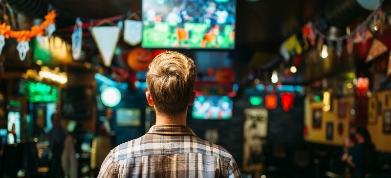 the back of a man standing in a bar watching the super bowl game