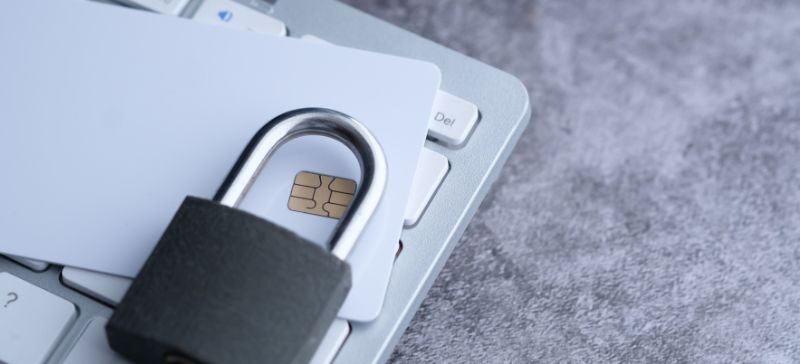 a padlock sits on top of a chip-enabled credit card and laptop