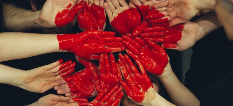 A group of hands together painted red to look like a heart