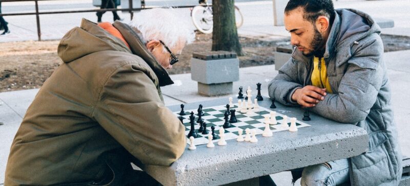 An old man and a young man playing chess in the park