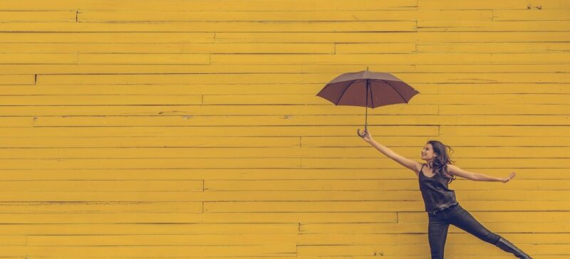 Woman jumping with an umbrella in front of a yellow background