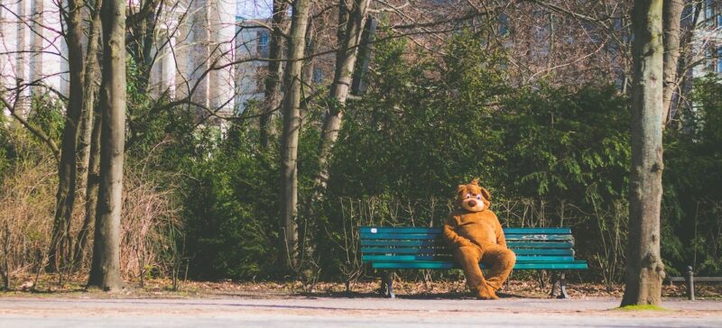 A person wearing a dog costume sitting on a bench in front of trees