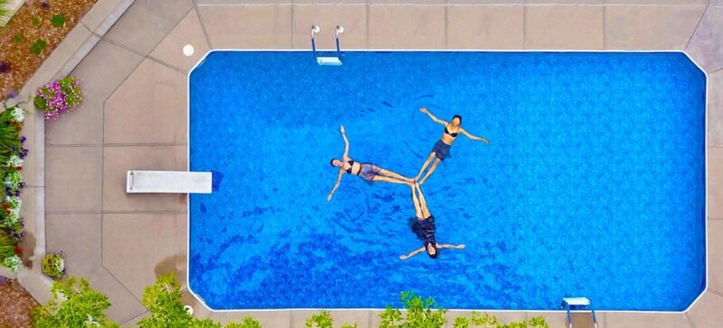 Three people swimming in a bright blue swimming pool