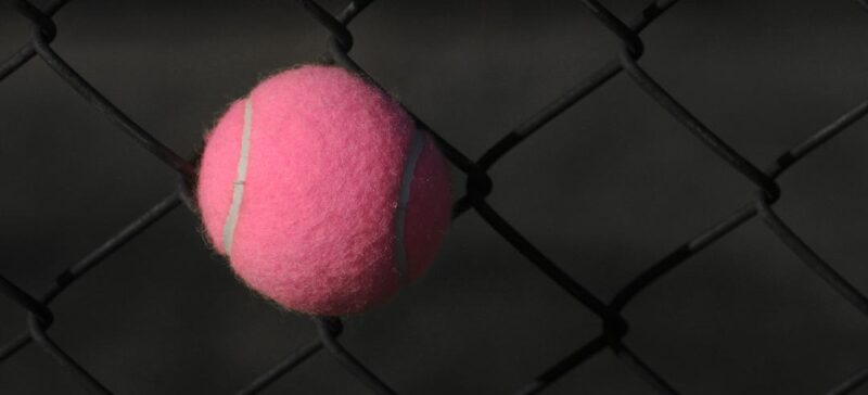 A pink tennis ball stuck in a chainlink fence