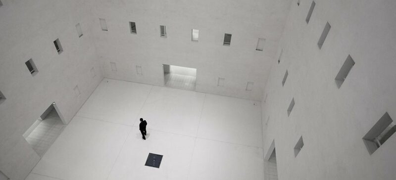 Man in a high-ceiling white room with three doors and many windows leading to other rooms.