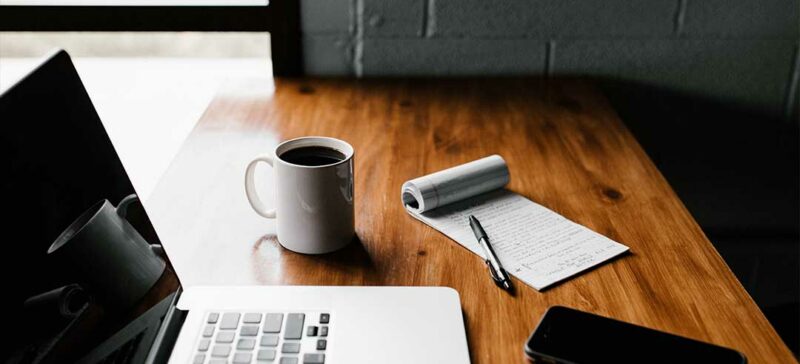 Laptop, mobile phone and coffee next to a notepad on a table