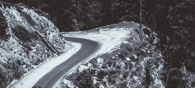 car driving on mountain road with hairpin turn ahead next to a sheer drop off