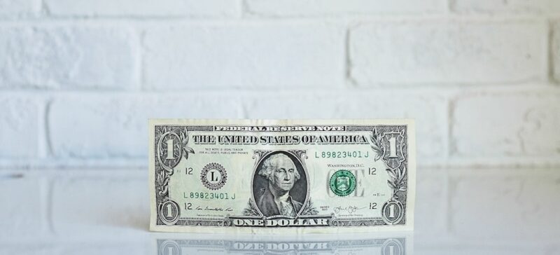 Dollar bill sitting on a white reflective counter in front of a white brick wall