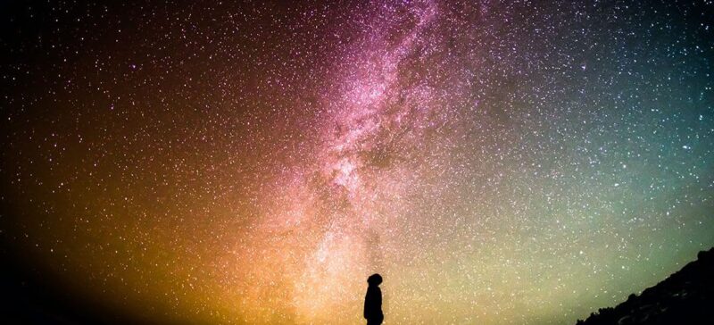 Man looking at a night sky that's filled with stars and brightly colored galaxy imagery