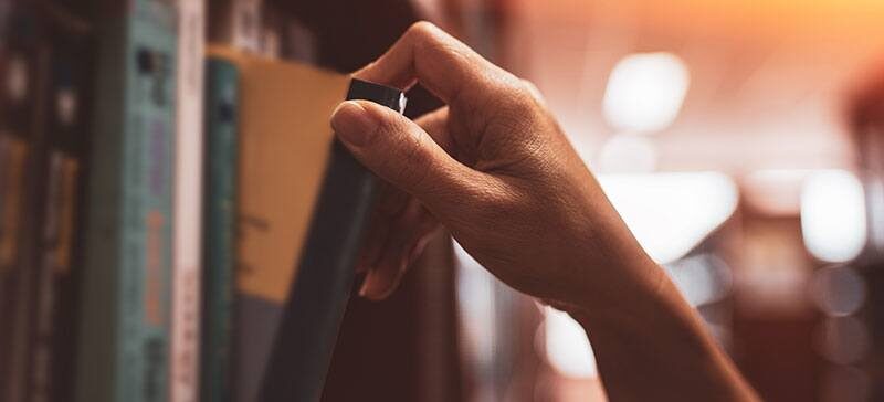 Woman’s hand pulling a book off of the bookshelf.