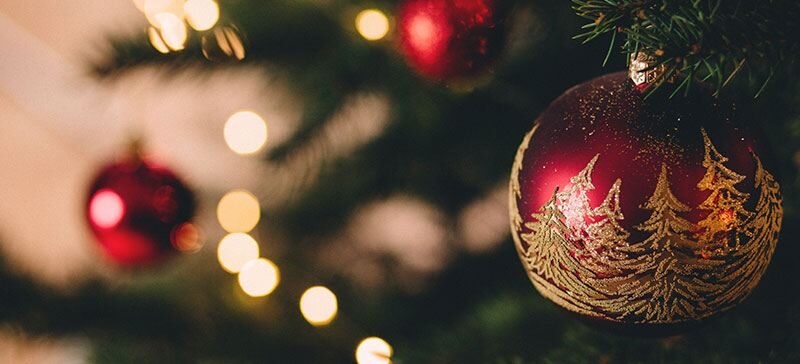 Gold and red Christmas ornament on a tree decorated with lights and other red ornaments.