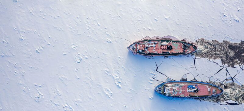 Two large ships side-by-side breaking through solid ice as they move forward