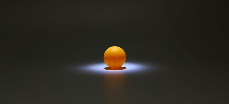 An orange ball sits in an empty, dimly lit room with a bright light shining down on it