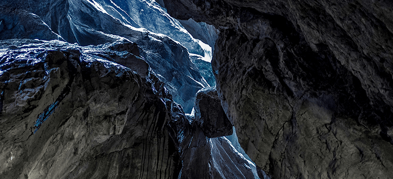 A dark fissure in a rocky cliff with a hint of cool light overhead, representing “gap” period between Acceleration and Maturation.